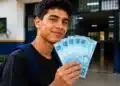 Jovem segurando cédulas de R$ 100, representando o pagamento do programa Pé-de-Meia, confirmado para junho, no valor de R$ 1.200.