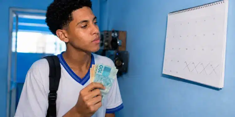 Estudante brasileiro conferindo o calendário e segurando dinheiro, ilustrando o depósito do benefício Pé-de-Meia em junho.