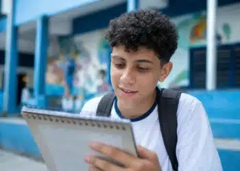 Estudante brasileiro em uniforme escolar olhando para um calendário, representando a consulta às datas de pagamento do programa em junho de 2026.