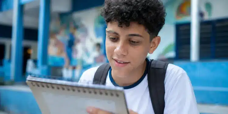 Estudante brasileiro em uniforme escolar olhando para um calendário, representando a consulta às datas de pagamento do programa em junho de 2026.