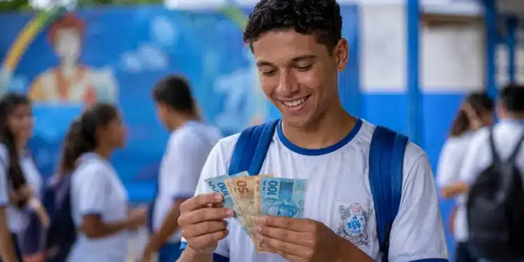 Estudante brasileiro de ensino médio segurando cédulas de reais em um pátio escolar, simbolizando recebimento de R$ 1.400 do Pé-de-Meia