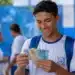Estudante brasileiro de ensino médio segurando cédulas de reais em um pátio escolar, simbolizando recebimento de R$ 1.400 do Pé-de-Meia