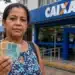 Mulher segurando dinheiro em frente a uma agência da Caixa Econômica Federal, representando a solicitação do valor de R$ 2.900 do PIS/Pasep