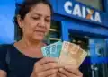 Mulher brasileira conferindo cédulas de dinheiro em frente a uma agência bancária, representando a solicitação do saque de R$ 2.900 do PIS/Pasep.