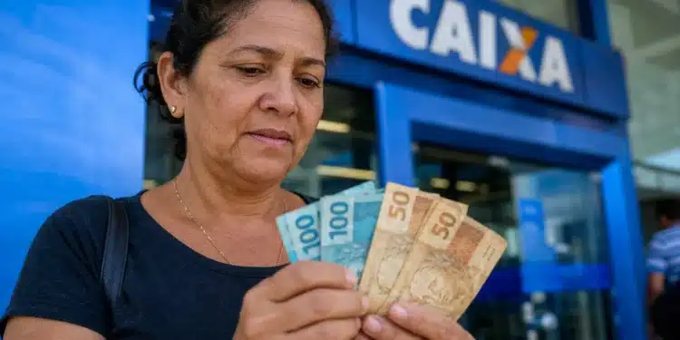 Mulher brasileira conferindo cédulas de dinheiro em frente a uma agência bancária, representando a solicitação do saque de R$ 2.900 do PIS/Pasep.