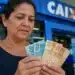Mulher brasileira conferindo cédulas de dinheiro em frente a uma agência bancária, representando a solicitação do saque de R$ 2.900 do PIS/Pasep.