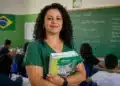 Professora brasileira em sala de aula pública segurando material didático, representando a valorização do piso salarial da educação básica.