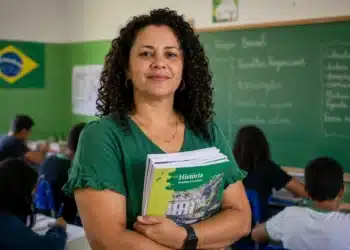 Professora brasileira em sala de aula pública segurando material didático, representando a valorização do piso salarial da educação básica.