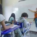 Professora explica conteúdo no quadro para estudantes em sala de aula da rede pública.