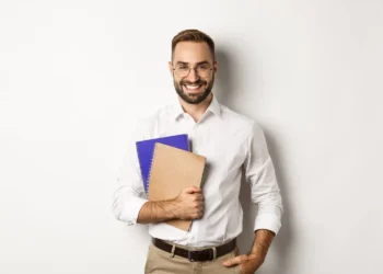 Homem sorridente segurando cadernos, representando estudante ou docente em contexto de preparação para a Prova Nacional Docente (PND).