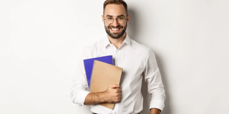 Homem sorridente segurando cadernos, representando estudante ou docente em contexto de preparação para a Prova Nacional Docente (PND).