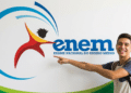 Estudante sorridente com mochila aponta para o logotipo do Enem em um painel