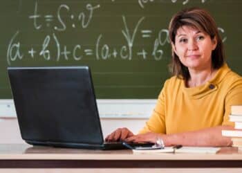 Professora ao computador em sala de aula representa as áreas avaliadas na Prova Nacional Docente 2026