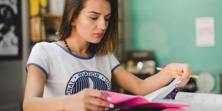 Estudante folheia caderno de anotações com lápis na mão durante sessão de estudos para o Enem