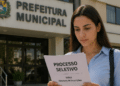 Mulher lendo edital de processo seletivo em frente à prefeitura municipal.