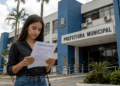 Mulher lendo edital de processo seletivo em frente ao prédio da Prefeitura Municipal.