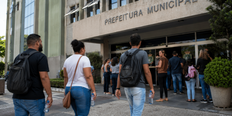 Pessoas em frente à prefeitura municipal aguardando atendimento em processo seletivo com vagas abertas.