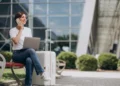 Mulher trabalhando remotamente em espaço externo com notebook sobre mala de viagem.