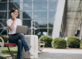Mulher trabalhando remotamente em espaço externo com notebook sobre mala de viagem.