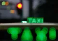 Taxi urbano iluminado à noite com letreiro verde “TAXI”, simbolizando o transporte por aplicativo e renovação de frota no programa Move Brasil.