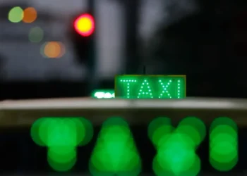 Taxi urbano iluminado à noite com letreiro verde “TAXI”, simbolizando o transporte por aplicativo e renovação de frota no programa Move Brasil.