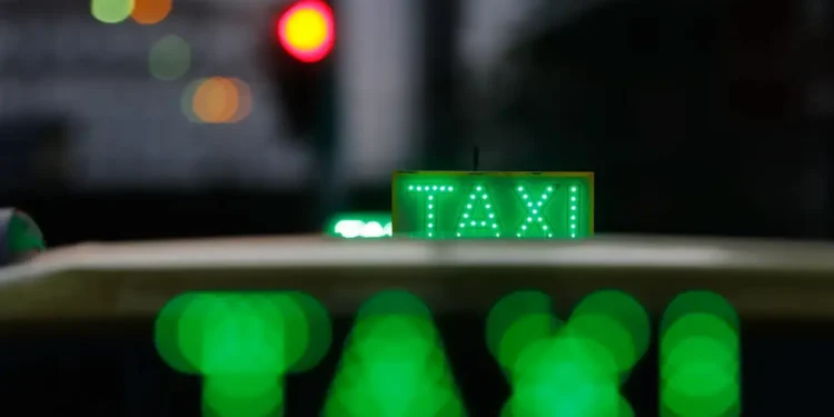 Taxi urbano iluminado à noite com letreiro verde “TAXI”, simbolizando o transporte por aplicativo e renovação de frota no programa Move Brasil.