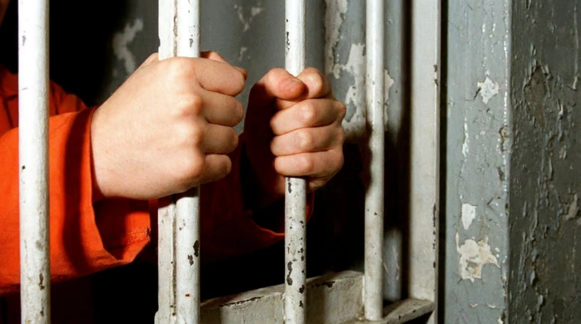 Mãos segurando grades de cela, representando o debate sobre responsabilização penal de adolescentes