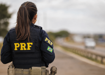 Agente da Polícia Rodoviária Federal de costas em rodovia.