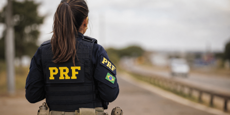 Agente da Polícia Rodoviária Federal de costas em rodovia.