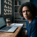 Jovem estudante sentado diante de um notebook sobre a mesa.