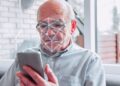 Idoso de óculos realiza reconhecimento facial pelo celular com malha de biometria sobre o rosto