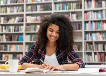 Estudante concentrada organizando estudos para o Enem 2026 em ambiente de biblioteca.
