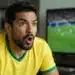 Torcedor brasileiro assiste à partida da Seleção Brasileira na TV, representando a expectativa pelo próximo jogo do Brasil na Copa do Mundo de 2026.