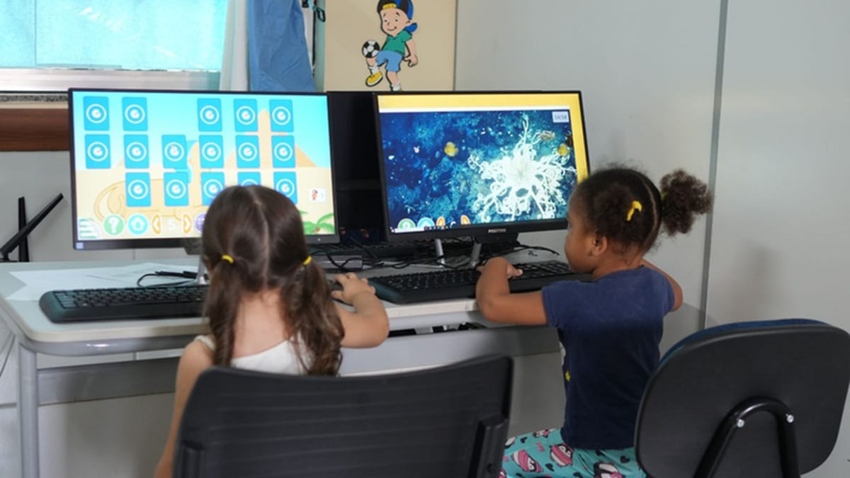 Duas crianças usam computadores com jogos educativos em sala de aula equipada com tecnologia