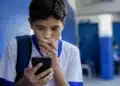 Adolescente usando smartphone em ambiente escolar, representando a proibição de redes sociais para menores de 15 anos