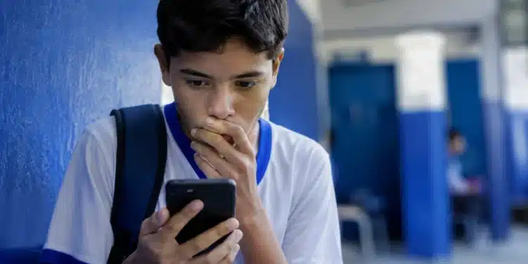 Adolescente usando smartphone em ambiente escolar, representando a proibição de redes sociais para menores de 15 anos