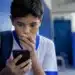 Adolescente usando smartphone em ambiente escolar, representando a proibição de redes sociais para menores de 15 anos