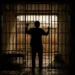 Silhueta de homem atrás das grades em cela, simbolizando a aprovação da redução da maioridade penal pela Comissão da Câmara.