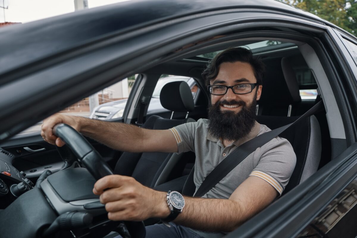 Motorista sorridente de óculos dirige com o cinto de segurança afivelado