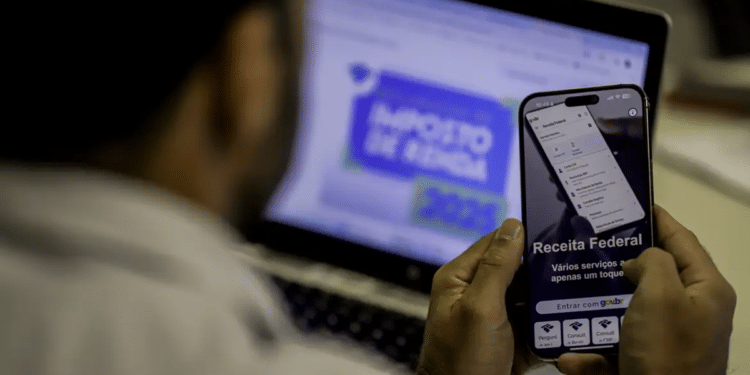 Contribuinte usa celular e notebook para acompanhar a restituição do Imposto de Renda.