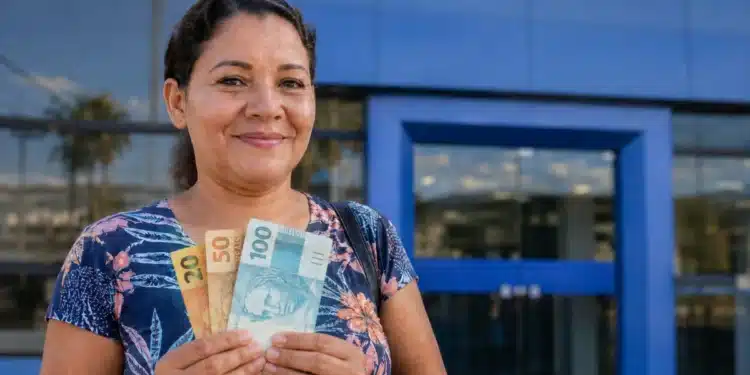 Mulher brasileira segurando cédulas de real em frente a uma agência bancária, simbolizando o pagamento da restituição do Imposto de Renda liberado pela Receita Federal.
