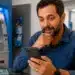 Pessoa utilizando smartphone dentro de agência bancária no Brasil, representando a consulta de informações sobre restituição automática do Imposto de Renda em 2026.