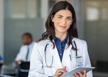 Médica com jaleco e tablet em ambiente hospitalar, representando as inscrições abertas para a primeira etapa do Revalida 2026/2.