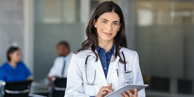 Médica com jaleco e tablet em ambiente hospitalar, representando as inscrições abertas para a primeira etapa do Revalida 2026/2.