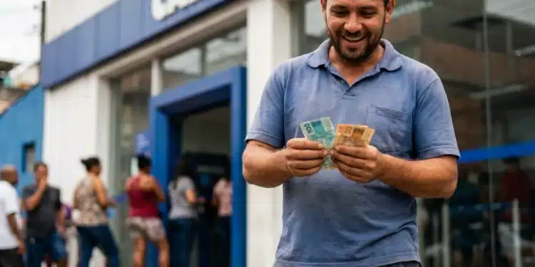 Homem sorridente contando dinheiro em frente à agência da Caixa Econômica Federal, representando o saque de R$ 6.220.