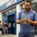 Homem sorridente contando dinheiro em frente à agência da Caixa Econômica Federal, representando o saque de R$ 6.220.