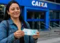 Mulher segurando notas de dinheiro em frente a uma agência da Caixa, representando o saque de R$ 6.220.