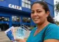 Mulher segurando documentos em frente a agência da Caixa, com dinheiro nas mãos, representando a solicitação do saque de R$ 6.220 para moradores das 9 cidades habilitadas.