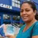 Mulher segurando documentos em frente a agência da Caixa, com dinheiro nas mãos, representando a solicitação do saque de R$ 6.220 para moradores das 9 cidades habilitadas.