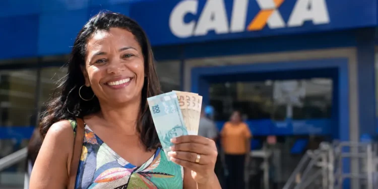Mulher sorri segurando notas de real em frente a uma agência da Caixa, ilustrando saque de R$ 3.950 do FGTS até 30 de junho